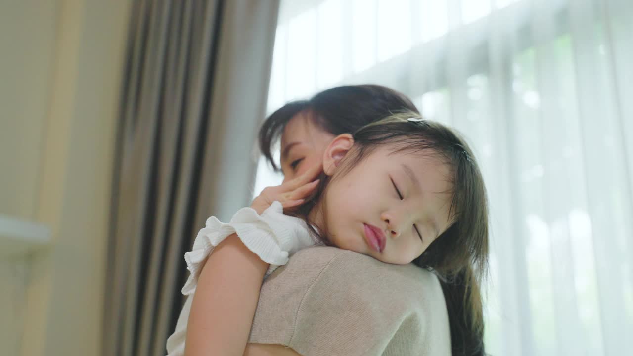 亚洲美丽慈爱的母亲抱着熟睡的女婴在她的臂弯温柔。父母微笑着站在小宝贝小女儿的肩膀上休息。家庭亲子关系概念。