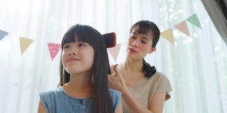 亚洲慈爱的母亲花闲暇时间与年轻的小女儿在客厅里。细心的妈妈用发刷轻柔地梳理着孩子的头发。家庭教养关系。