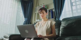 快乐的亚洲女商人因新冠肺炎疫情在家办公，通过手机与同事交流工作项目。自由职业者女孩使用电脑，喜欢在家里通过互联网交流。