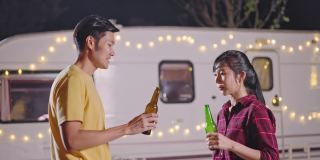 亚洲年轻男女旅行者朋友正在举行户外节日聚会。夫妻俩一起喝一瓶啤酒，晚上一起开怀大笑。旅行自然，露营车露营。