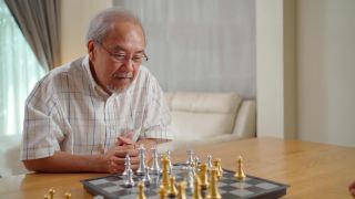 亚洲老年男性花休闲时间，退休后呆在家里。快乐的微笑老人喜欢在家里和朋友一起下棋。医院保健和医疗理念视频素材模板下载