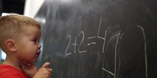 穿红衬衫的小男孩在黑板上写数学数字