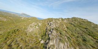 从高空俯瞰，高速飞过被绿色植被覆盖的山脉，远处是地中海。意大利撒丁岛。FPV无人机，登山冲浪。