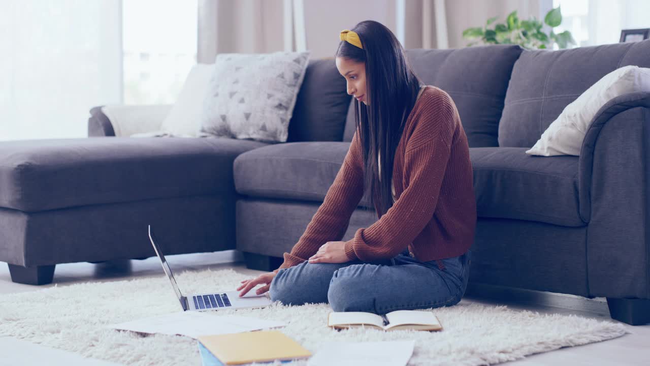 一名年轻女子坐在休息室地板上使用笔记本电脑的4k视频，周围是笔记和表格