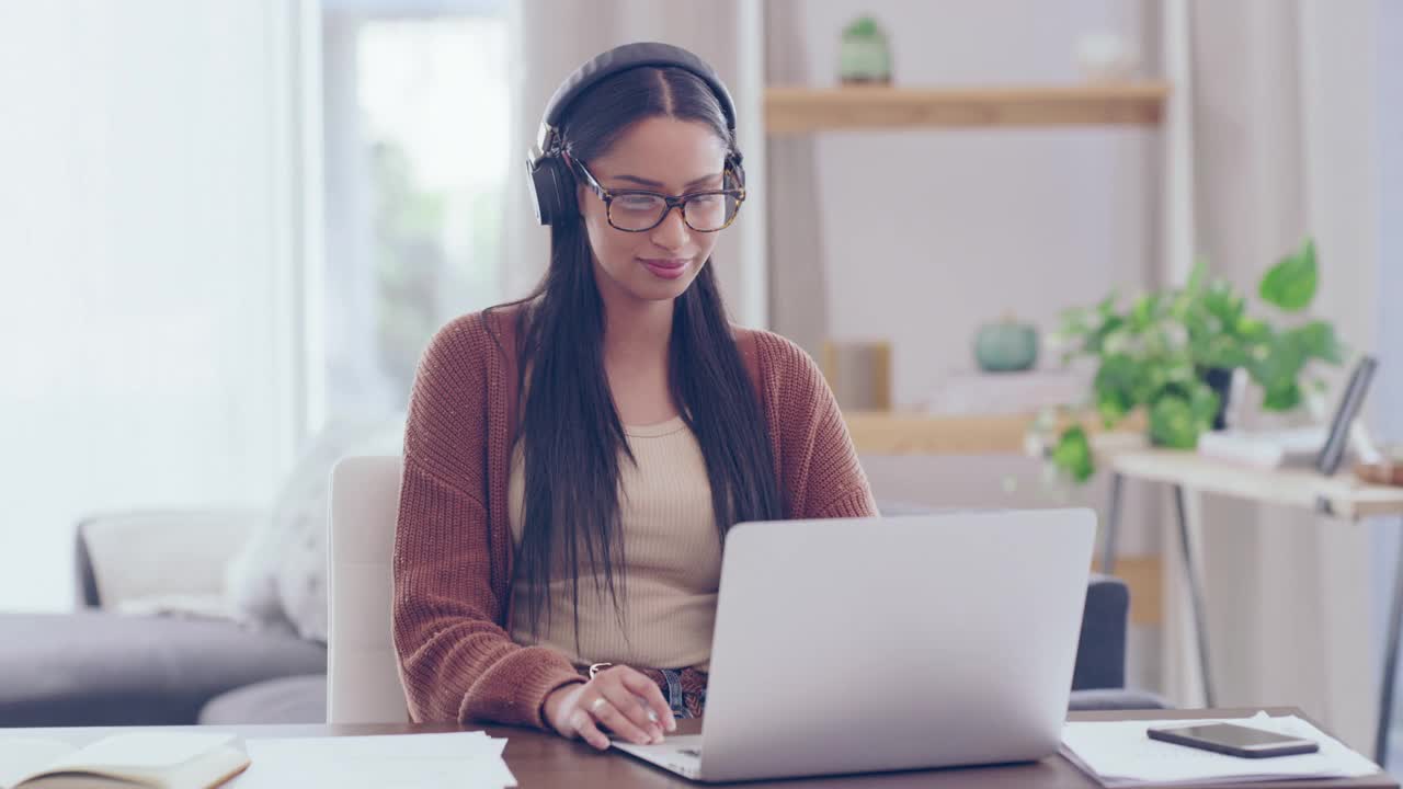 一名年轻女子戴着耳机边唱歌边用笔记本电脑在家完成文书工作的4k视频
