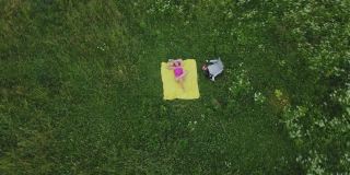 一个女人在绿色的草地上晒太阳。他趴在一张黄色的地毯上。航空摄影。