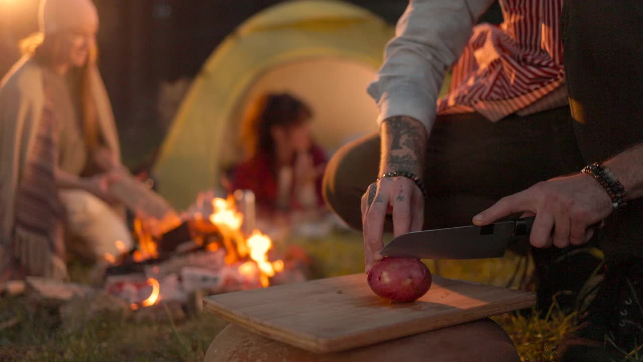 一个面目全非的男人在和朋友们露营时切土豆当晚餐。
