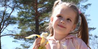 快乐可爱的小女孩香蕉水果。户外散步，健康饮食理念。