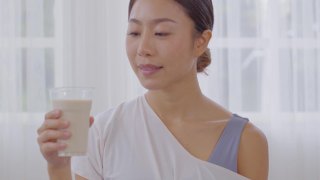 健康的年轻亚洲妇女在家里喝牛奶与钙强壮骨骼，微笑的印度妇女拿着玻璃豆浆享受营养健康的生活，健康与天然牛奶新鲜的概念视频素材模板下载