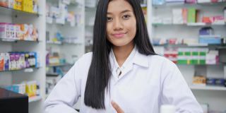 女医生面试介绍和在药店工作。亚洲药剂师女孩建议在药店使用有药学背景的货架药品。看着镜头。