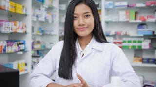女医生面试介绍和在药店工作。亚洲药剂师女孩建议在药店使用有药学背景的货架药品。看着镜头。视频素材模板下载