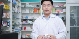 亚洲药师在医院药房的网上展示和会议。亚洲男子医生建议使用药物和看着摄像机。有药店药学背景的货架。