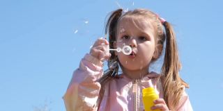 快乐的小女孩吹肥皂泡。活泼的孩子在公园散步。家庭生活方式，户外活动，和孩子一起度假。慢动作
