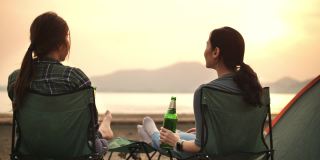 两个露营的女人喝着啤酒享受日落，看着美丽的山