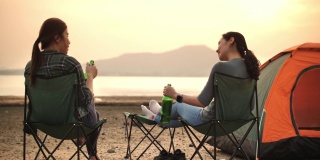 两个露营的女人喝着啤酒享受日落，看着美丽的山