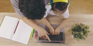 俯视图4K可爱的亚洲女孩的孩子，戴着耳机和手打字键盘，正在网上学习从电脑笔记本电脑与她的父亲教学显示父母支持教育在家里。