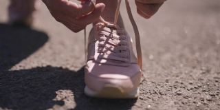 高级女性双手系鞋带，穿着粉色运动鞋离开。在阳光明媚的夏日户外慢跑跑步的白人退休人员的特写。慢动作