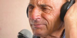 老年人在家的悠闲。一位白种老人戴着耳机，用麦克风深情地唱着歌。老年人唱卡拉ok的肖像。快乐的老人在唱歌。