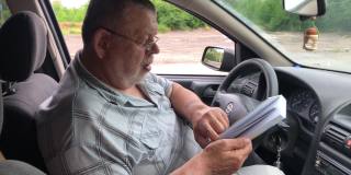 一个白人老人坐在驾驶座上看书