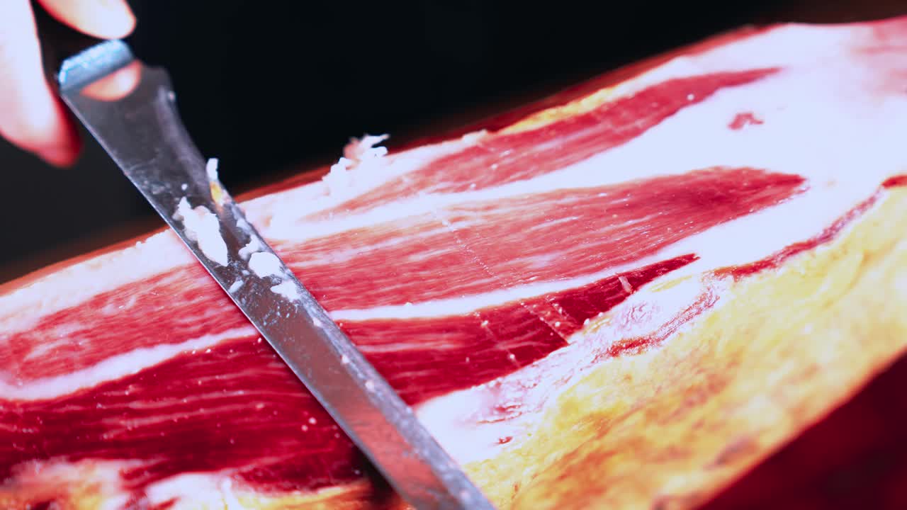 一个匿名的人正在切一个100%伊比利亚火腿腿，用镊子夹着一片可口的伊比利亚火腿。Acorn-fed伊比利亚火腿。典型的西班牙或加泰罗尼亚食物。伊比利亚猪肉。