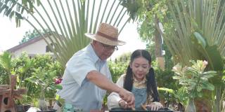 亚洲退休的爷爷和漂亮的孙女一起在家里的花园里帮忙种树。愉快享受假期的家庭户外活动。