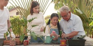 亚洲父母，漂亮的女儿，和爷爷一起在家里的花园里帮忙种树。愉快享受假期的家庭户外活动。