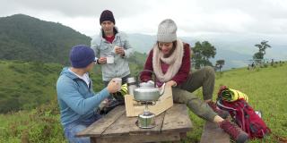一群亚洲朋友一起在山上露营，坐在户外椅子上喝着热咖啡