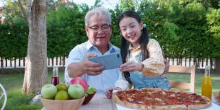 亚洲退休的爷爷和漂亮的孙女在家里的花园里享受着披萨。有家庭观念的退休老人快乐生活。