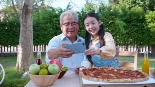 亚洲退休的爷爷和漂亮的孙女在家里的花园里享受着披萨。有家庭观念的退休老人快乐生活。视频素材模板下载