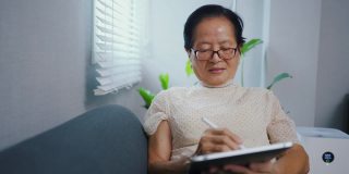 亚洲资深女性独自在家使用平板电脑。