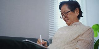 亚洲资深女性独自在家使用平板电脑。