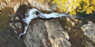 从上到下鸟瞰小山涧与快速移动的清澈的水之间的石头在秋天。