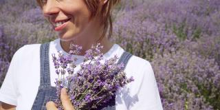 迷人的微笑的女人拿着花束站在薰衣草田。白人女士享受阳光灿烂的夏天在鲜花草地上。幸福和女性的概念。
