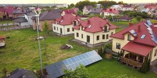 鸟瞰图郊区住宅和私人住宅的绿草覆盖的院子，屋顶上的太阳能电池板，游泳池与蓝色的水和风力发电机。