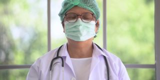 肖像的亚洲女医生脱下脸痕和微笑与幸福的生活。医疗保健产业的工人生活。老年人站在室内，以自然、树木和阳光为背景。