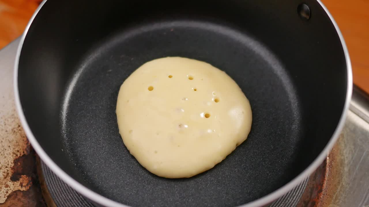 自制的煎饼在不粘锅上做美味的早餐。女性的手用锅铲在热锅上翻动煎饼。
