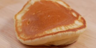 双手将蜂蜜倒在美味的薄饼上。香甜的自制煎饼配蜂蜜或糖浆做早餐。