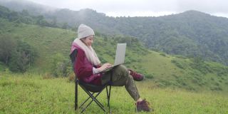 4K亚洲女人坐在山上用笔记本电脑工作