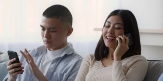 亚洲夫妇在家里使用智能手机和通过电话交谈