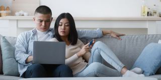 不满的亚洲夫妇在家里使用笔记本电脑和信用卡