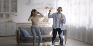 年轻的亚洲夫妇戴着耳机在家里跳舞