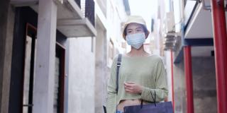 亚洲妇女戴着口罩，提着纸袋在城市里购物。戴上口罩，防止新冠肺炎的传播和保持社交距离
