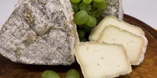 一盘混合的发霉的山羊奶奶酪放在一块木板上，上面还有绿色的葡萄