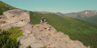 鸟瞰图一个年轻的男运动员坐在悬崖的边缘，眺望远方。展望未来。徒步者在爬到山顶时在山上休息