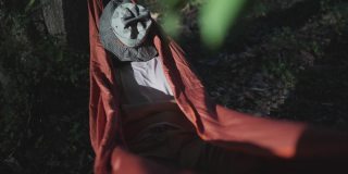 一名男子在露营时用帽子遮住脸，睡在吊床上