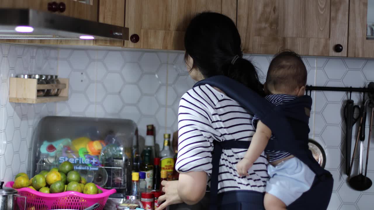 女人在厨房做饭，婴儿用吊带绑在身上
