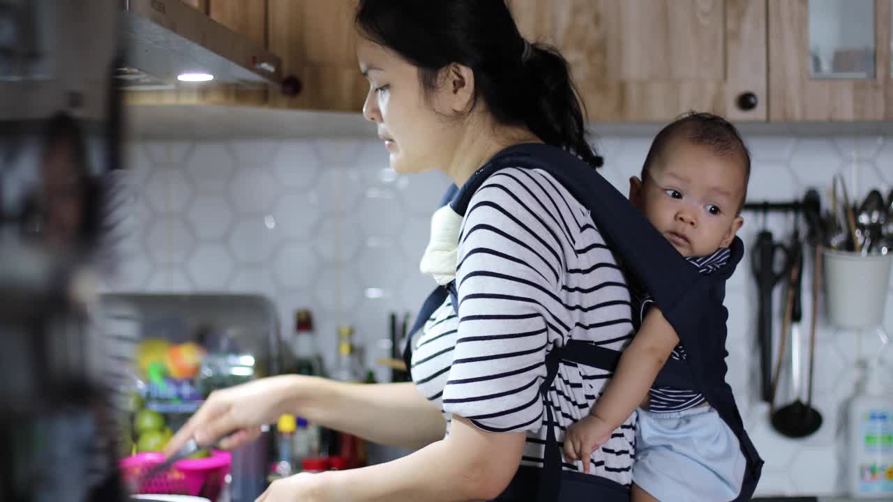 女人在厨房做饭，婴儿用吊带绑在身上