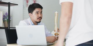 慢动作场景专业理疗师为患者讲解下背部人体骨骼脊柱解剖，为患者在办公室治疗提供医疗保健概念咨询