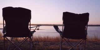 一对游客椅，一个折叠椅，在河边的背景下，美丽的夕阳，放松和休息，享受与自然的统一。