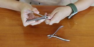 亚洲妇女在家里的木桌上用指甲钳剪指甲